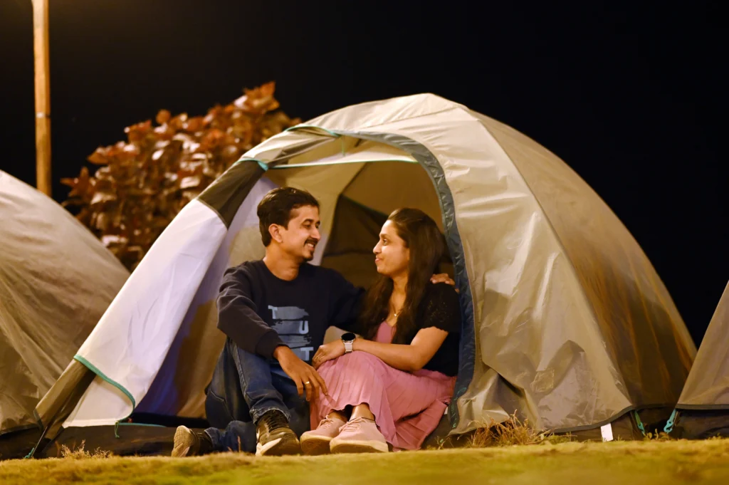 A couple sitting together outside a tent, smiling at each other in a nighttime setting.