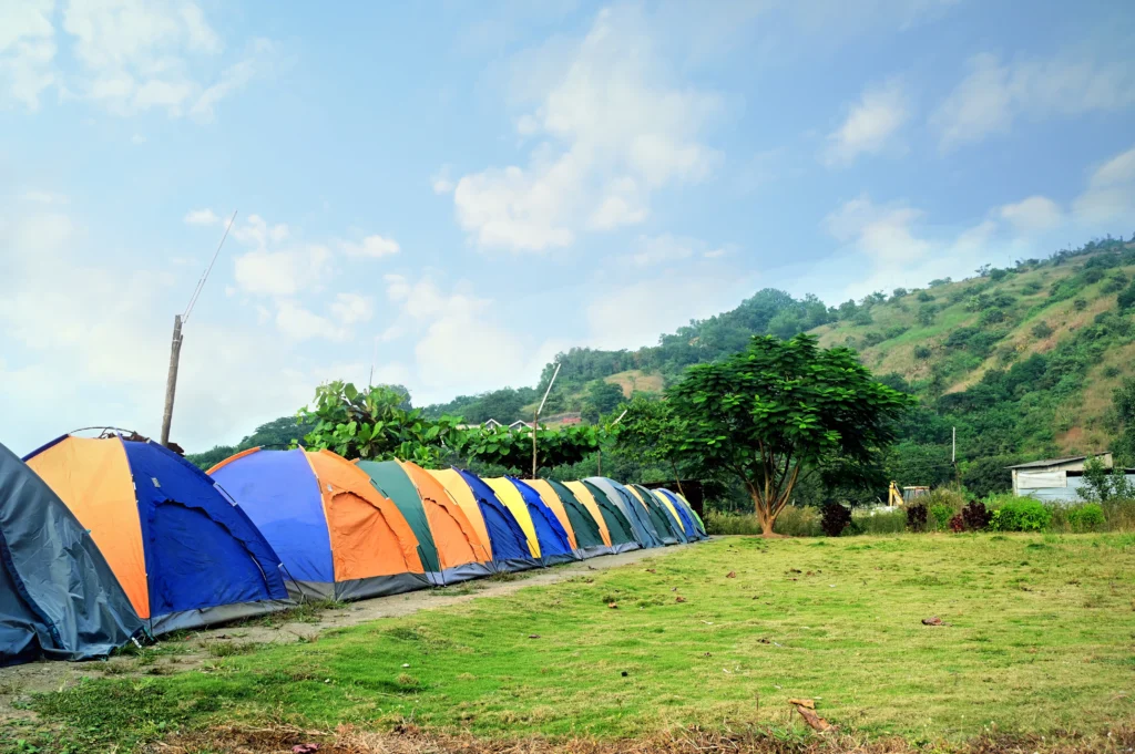 A row of colorful camping tents set up on a grassy area with a hillside in the background.