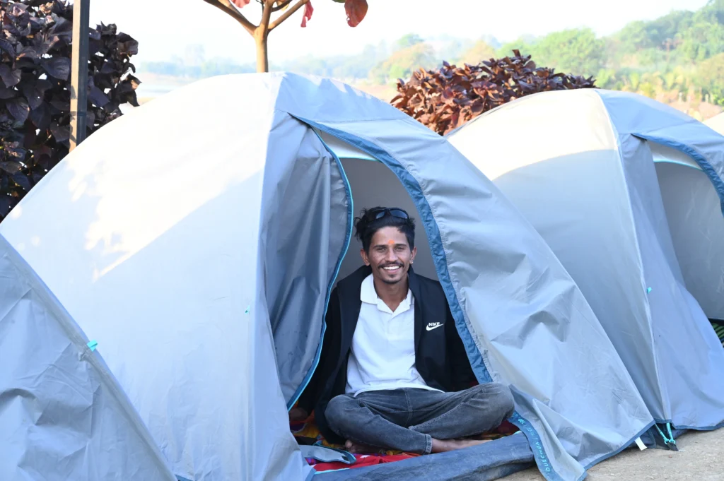 A man sitting inside a gray tent with a relaxed expression, wearing casual clothing.